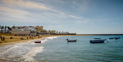 Playa de la Caleta con las embarcaciones en la orilla y el edificio del balneario