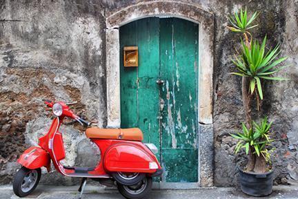 Vespa roja aparcada junto a una colorida puerta