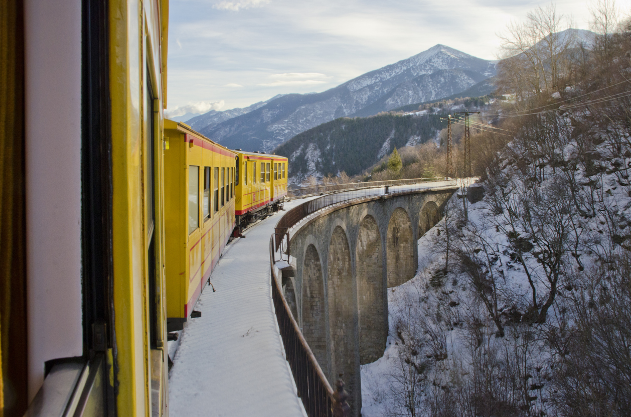 Tren amarillo pasando sobre un puente en un paisaje nevado