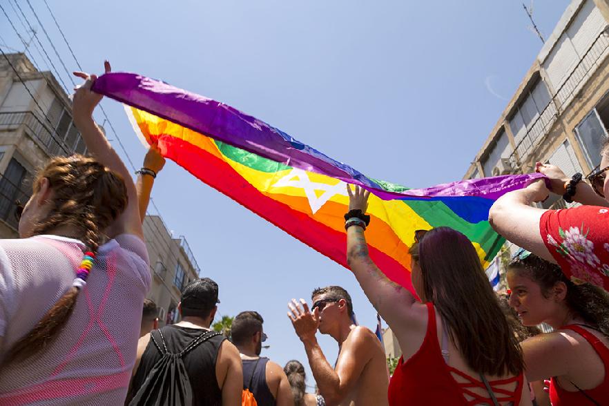 Participantes desfilando con la bandera arcoíris por la ciudad